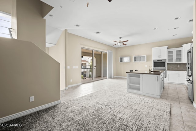 kitchen with white cabinets, light tile patterned floors, ceiling fan, stainless steel appliances, and a center island with sink