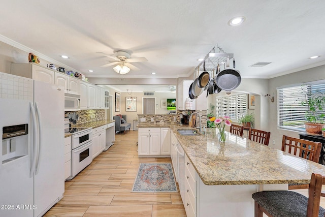 kitchen featuring white appliances, ornamental molding, a peninsula, and a sink