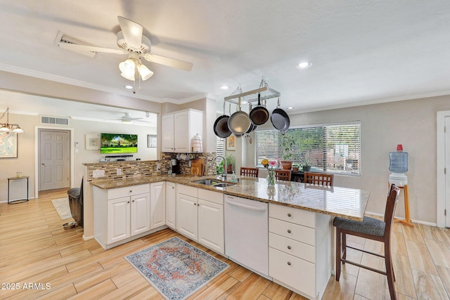 kitchen featuring white cabinetry, a sink, visible vents, white dishwasher, and a peninsula