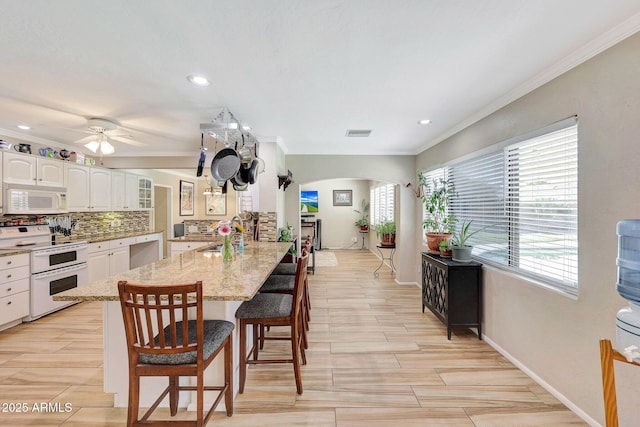 kitchen featuring a sink, a breakfast bar area, a peninsula, white appliances, and arched walkways