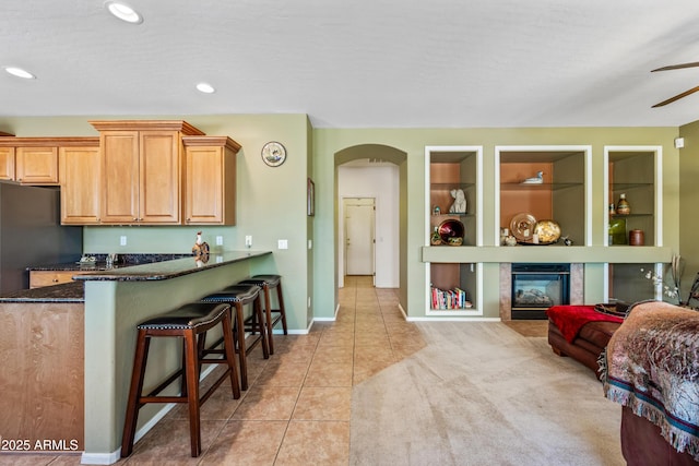 7342 E Norwood St, Mesa, AZ 85207 - kitchen featuring light tile patterned floors, a ceiling fan, a breakfast bar area, arched walkways, and dark stone countertops