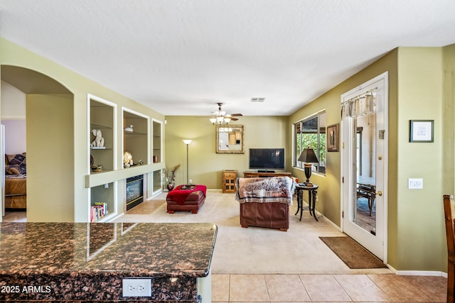 7342 E Norwood St, Mesa, AZ 85207 - tiled living area featuring carpet flooring, ceiling fan, a glass covered fireplace, arched walkways, and built in features