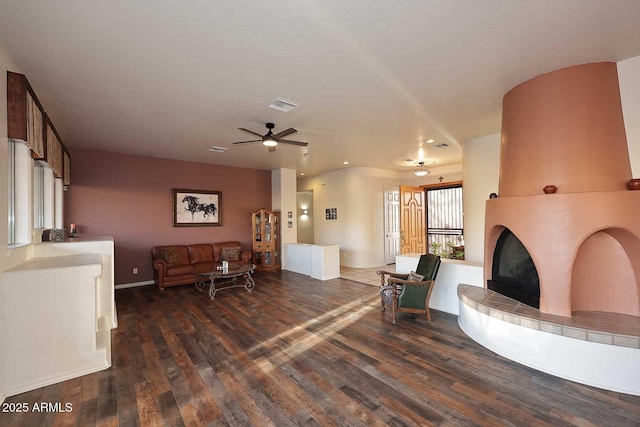 living room featuring a tiled fireplace, dark wood finished floors, visible vents, and a ceiling fan