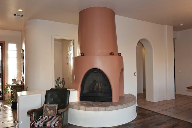 living area featuring dark wood-style floors, a tile fireplace, visible vents, and arched walkways