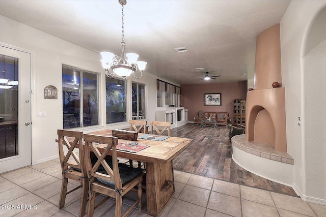 tiled dining area featuring a textured ceiling, ceiling fan with notable chandelier, visible vents, and baseboards