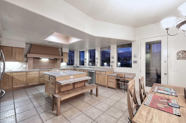 kitchen featuring light tile patterned floors, tile counters, backsplash, wall chimney range hood, and dishwasher