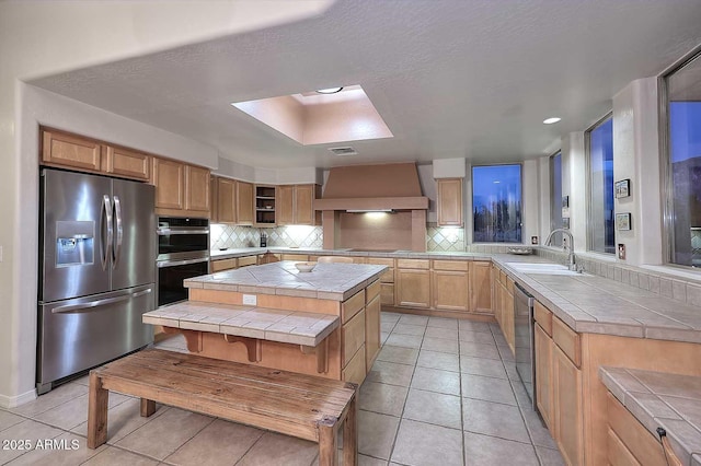 kitchen featuring stainless steel appliances, a center island, tile countertops, and wall chimney range hood