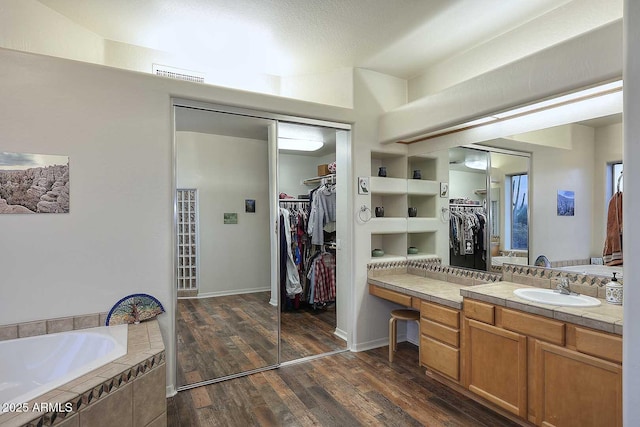 full bathroom with visible vents, wood finished floors, a garden tub, a walk in closet, and vanity