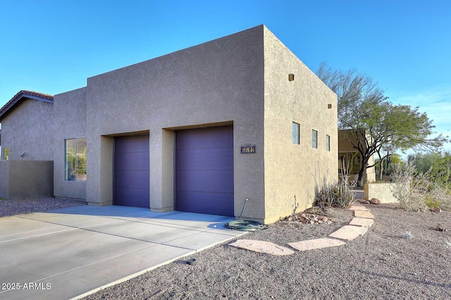 view of side of home featuring driveway, an attached garage, and stucco siding