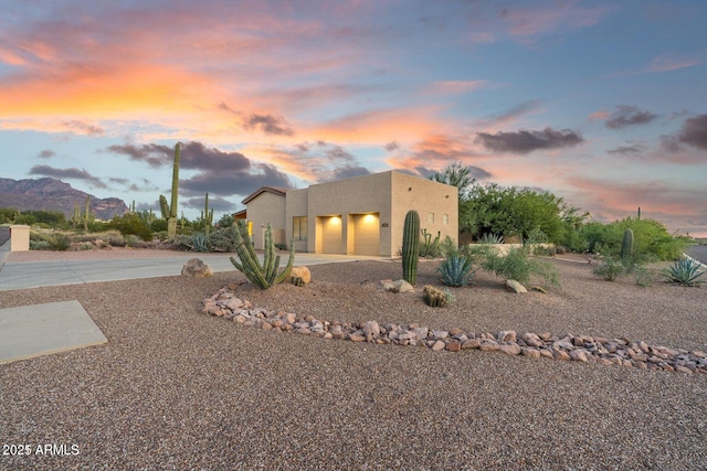 pueblo revival-style home with a garage, a mountain view, driveway, and stucco siding