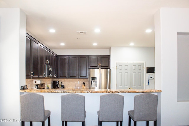 15148 W Sells Dr, Goodyear, AZ 85395 - kitchen featuring appliances with stainless steel finishes, dark brown cabinets, a breakfast bar area, decorative backsplash, and a peninsula