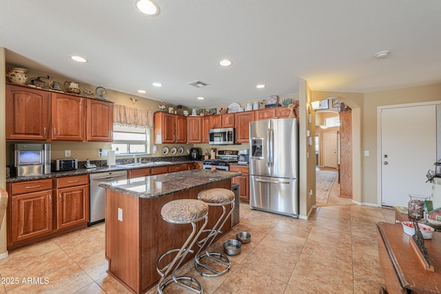 44890 W Desert Garden Rd, Maricopa, AZ 85139 - kitchen featuring appliances with stainless steel finishes, arched walkways, a center island, a sink, and brown cabinetry