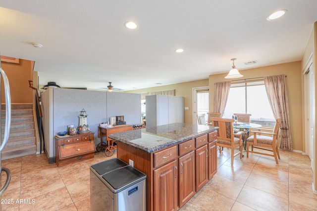 44890 W Desert Garden Rd, Maricopa, AZ 85139 - kitchen with brown cabinetry, a kitchen island, ceiling fan, dark stone counters, and pendant lighting
