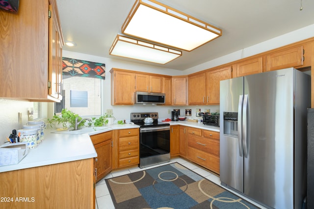 kitchen with sink, appliances with stainless steel finishes, a skylight, and light tile patterned flooring