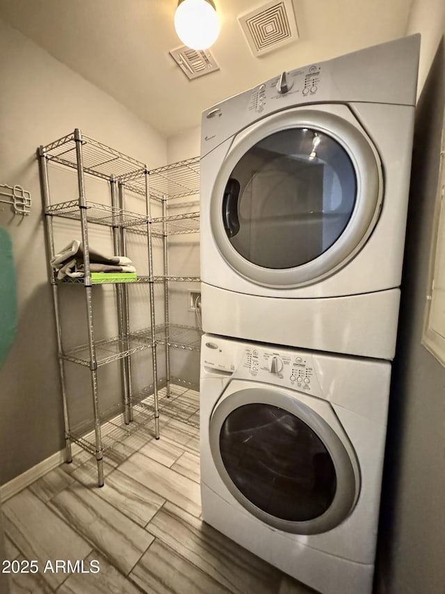 clothes washing area with laundry area, visible vents, and stacked washer / drying machine