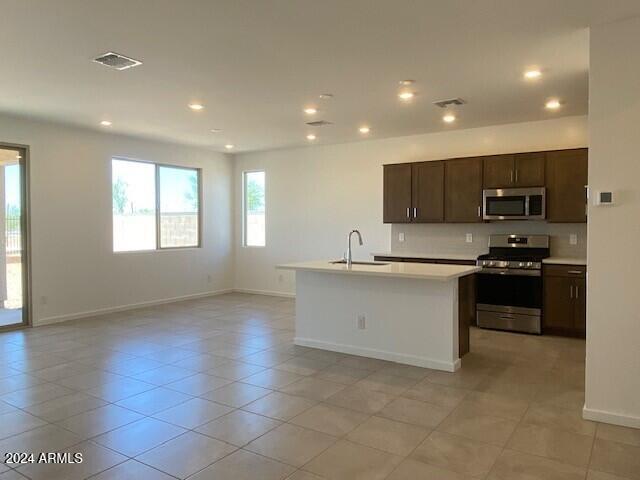 kitchen featuring an island with sink, stainless steel appliances, sink, dark brown cabinetry, and light tile patterned floors