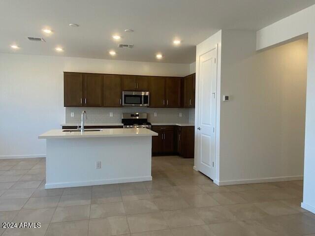 kitchen featuring sink, an island with sink, light tile patterned flooring, dark brown cabinets, and stainless steel appliances