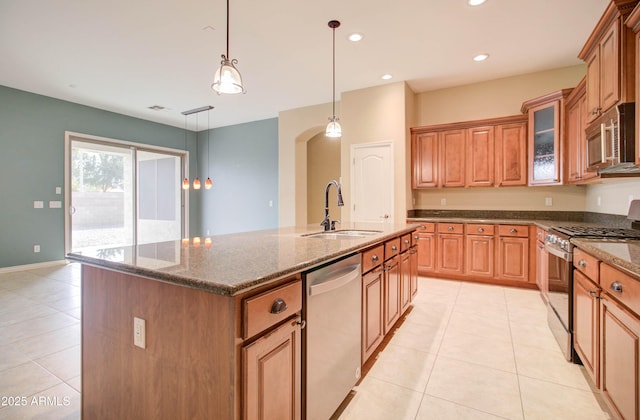 kitchen with sink, decorative light fixtures, dark stone countertops, appliances with stainless steel finishes, and an island with sink