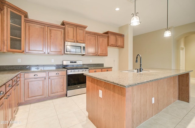 kitchen with appliances with stainless steel finishes, sink, a kitchen island with sink, light tile patterned floors, and light stone counters