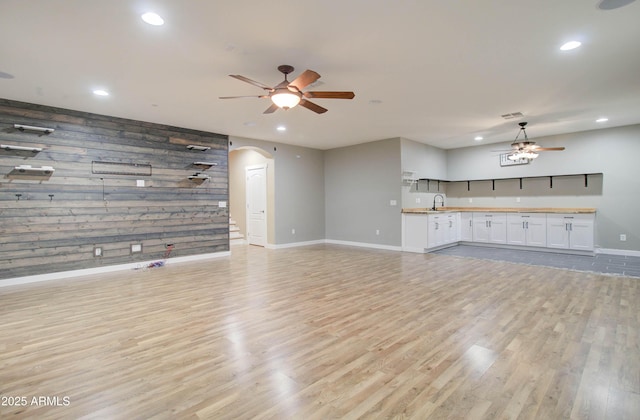 unfurnished living room featuring sink, light hardwood / wood-style floors, ceiling fan, and wood walls