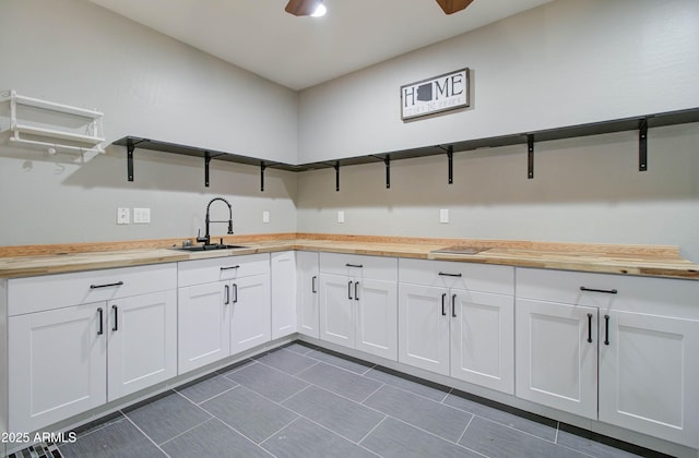 kitchen featuring butcher block counters, sink, white cabinetry, and ceiling fan