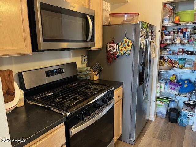 kitchen featuring light wood finished floors, light brown cabinetry, appliances with stainless steel finishes, and dark countertops