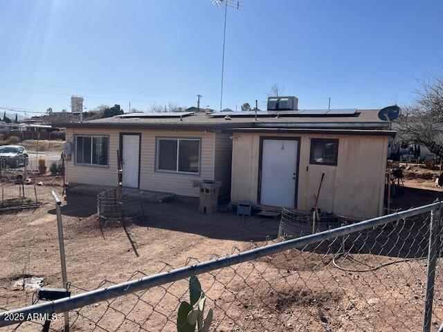 back of property featuring central AC unit, fence private yard, and roof mounted solar panels