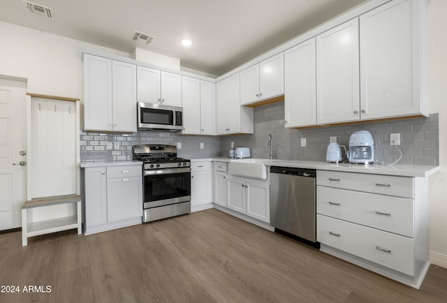 kitchen with decorative backsplash, white cabinets, light hardwood / wood-style flooring, sink, and stainless steel appliances