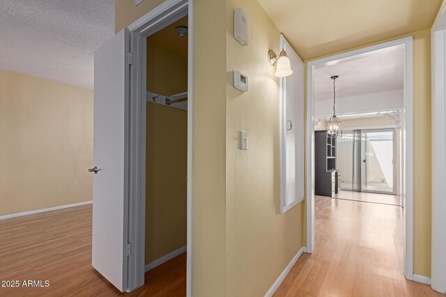 hall with wood finished floors, baseboards, and a textured ceiling