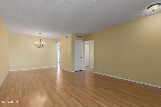 spare room featuring visible vents, baseboards, a notable chandelier, and light wood finished floors