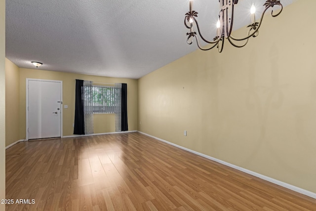 unfurnished room with a notable chandelier, baseboards, a textured ceiling, and light wood finished floors