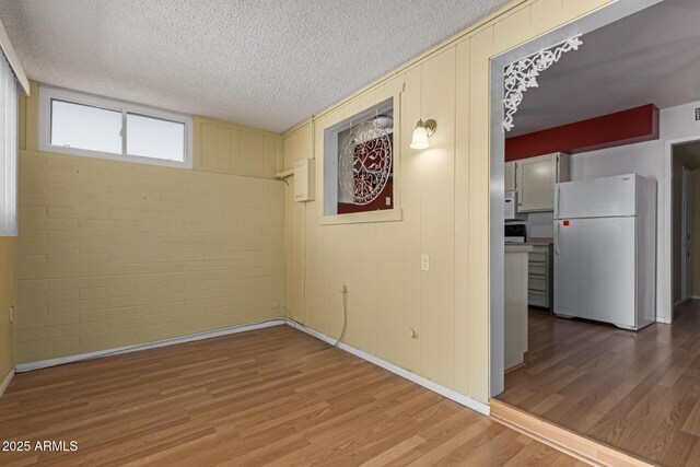 below grade area featuring a textured ceiling, wood finished floors, and freestanding refrigerator