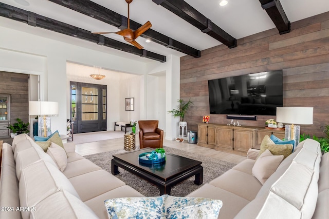 living room featuring light wood-type flooring, ceiling fan, beamed ceiling, and wood walls