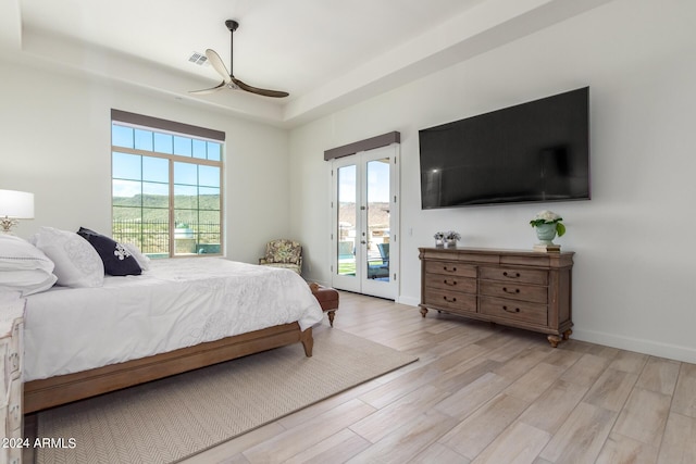 bedroom with french doors, access to outside, ceiling fan, a tray ceiling, and light hardwood / wood-style flooring