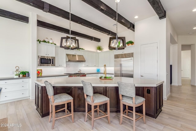 kitchen featuring a kitchen breakfast bar, a large island with sink, built in appliances, and hanging light fixtures