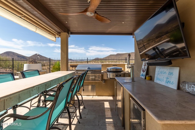 view of patio featuring an outdoor bar, ceiling fan, wine cooler, a mountain view, and an outdoor kitchen