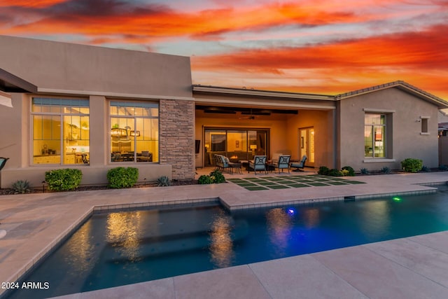 pool at dusk featuring ceiling fan and a patio