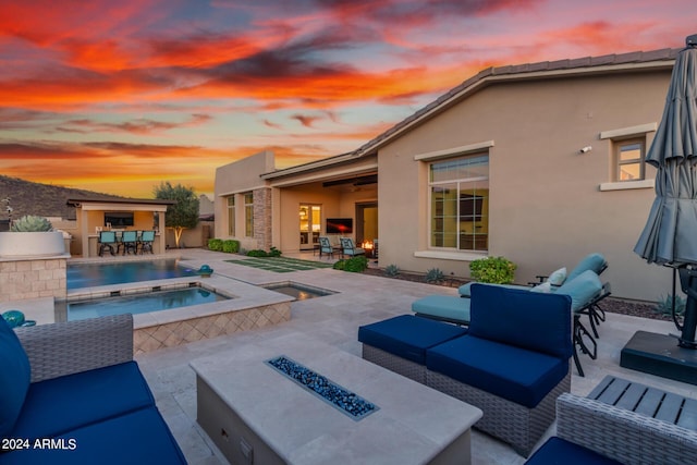 pool at dusk featuring an in ground hot tub, exterior bar, a patio, and an outdoor living space with a fire pit