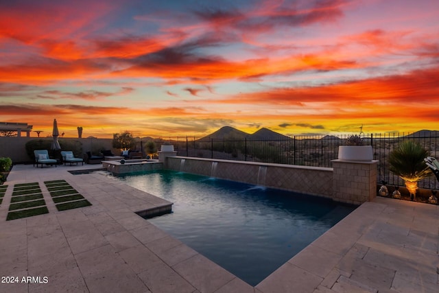 pool at dusk with a patio area and pool water feature