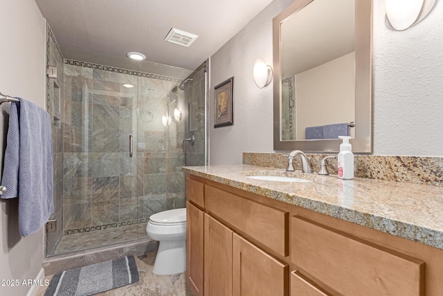 bathroom with a textured wall, toilet, vanity, visible vents, and a shower stall