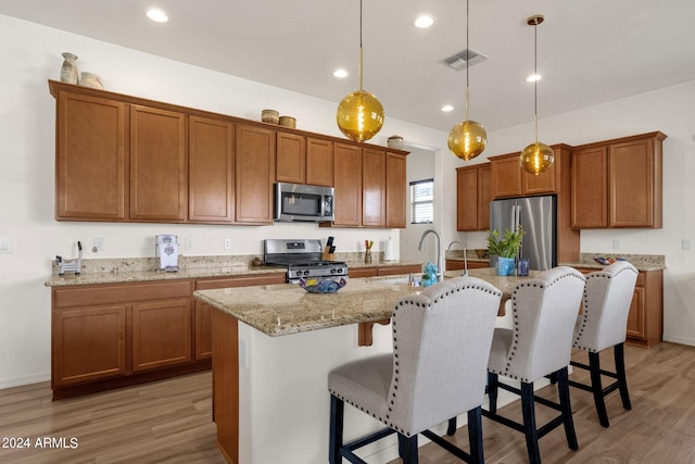 kitchen with hanging light fixtures, stainless steel appliances, sink, and an island with sink