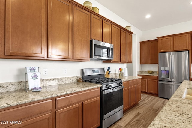 kitchen with light stone countertops, light wood-type flooring, and stainless steel appliances