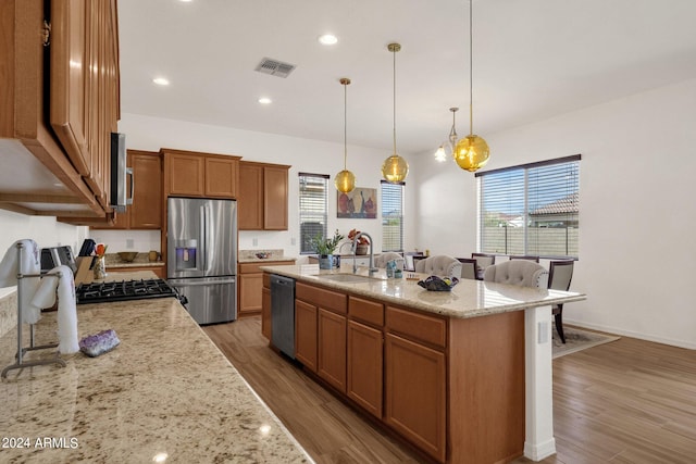 kitchen featuring an island with sink, stainless steel appliances, hardwood / wood-style floors, decorative light fixtures, and sink