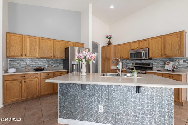 kitchen featuring sink, stainless steel appliances, high vaulted ceiling, a breakfast bar area, and a center island with sink