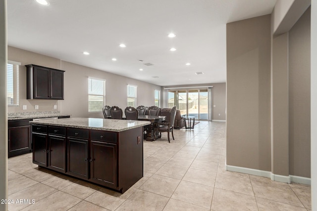 kitchen featuring light stone counters, dark brown cabinets, light tile patterned floors, and a kitchen island