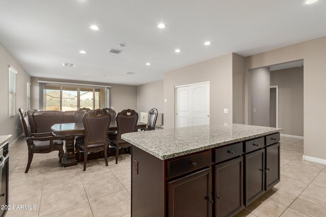 kitchen with dark brown cabinetry, light stone counters, a center island, and light tile patterned floors