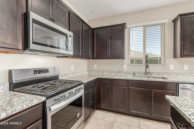 kitchen featuring light stone countertops, appliances with stainless steel finishes, dark brown cabinets, sink, and light tile patterned floors