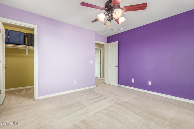 unfurnished bedroom with light colored carpet, ceiling fan, a closet, and a walk in closet