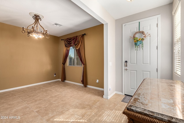 foyer entrance featuring a notable chandelier, light tile patterned flooring, and a healthy amount of sunlight