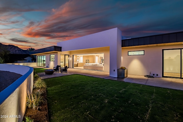 back house at dusk featuring a lawn, a patio area, and a mountain view